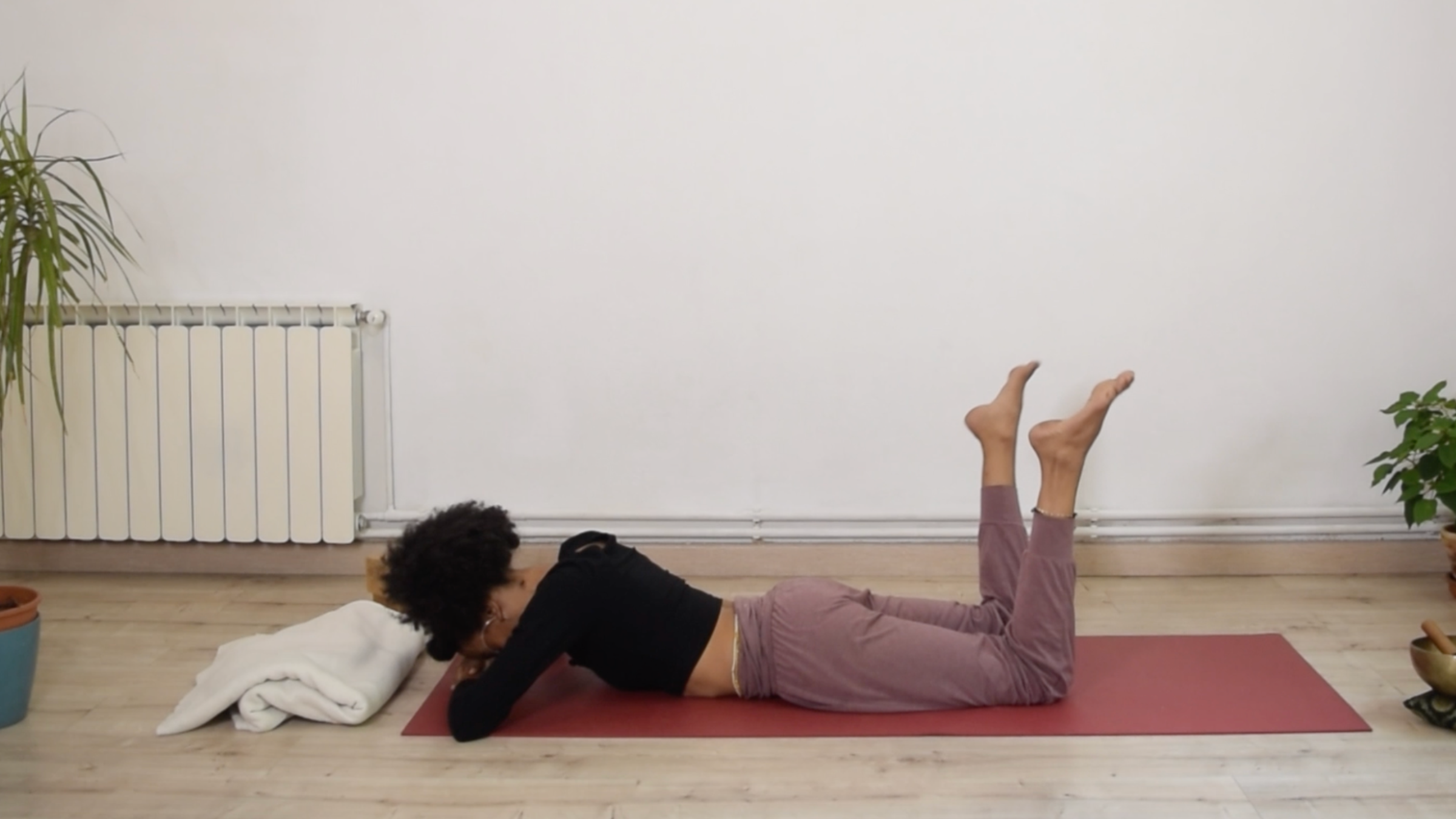 Yoga instructor Laia Bové lying on her stomach with knees bent, swaying her feet side to side in Prone Windshield Wipers.